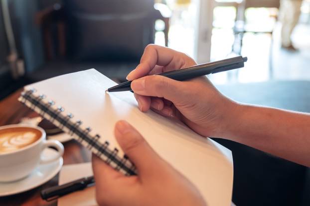 Closeup image of a woman's hands holding and writing down on a w