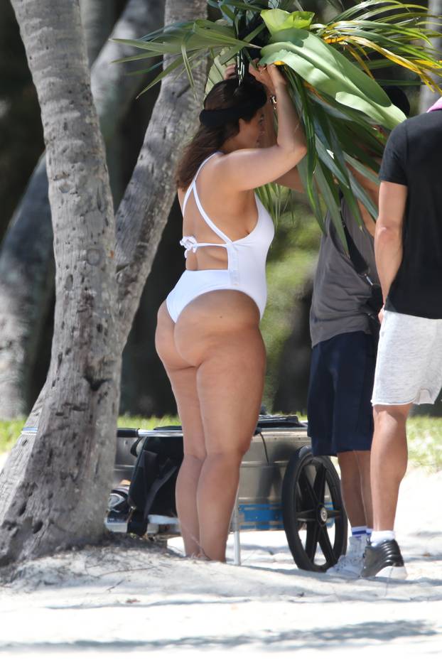 Ashley Graham shows off her curves in a white swimsuit and giant palm leaf headpiece as she takes part in a photo shoot for Glamour Magazine