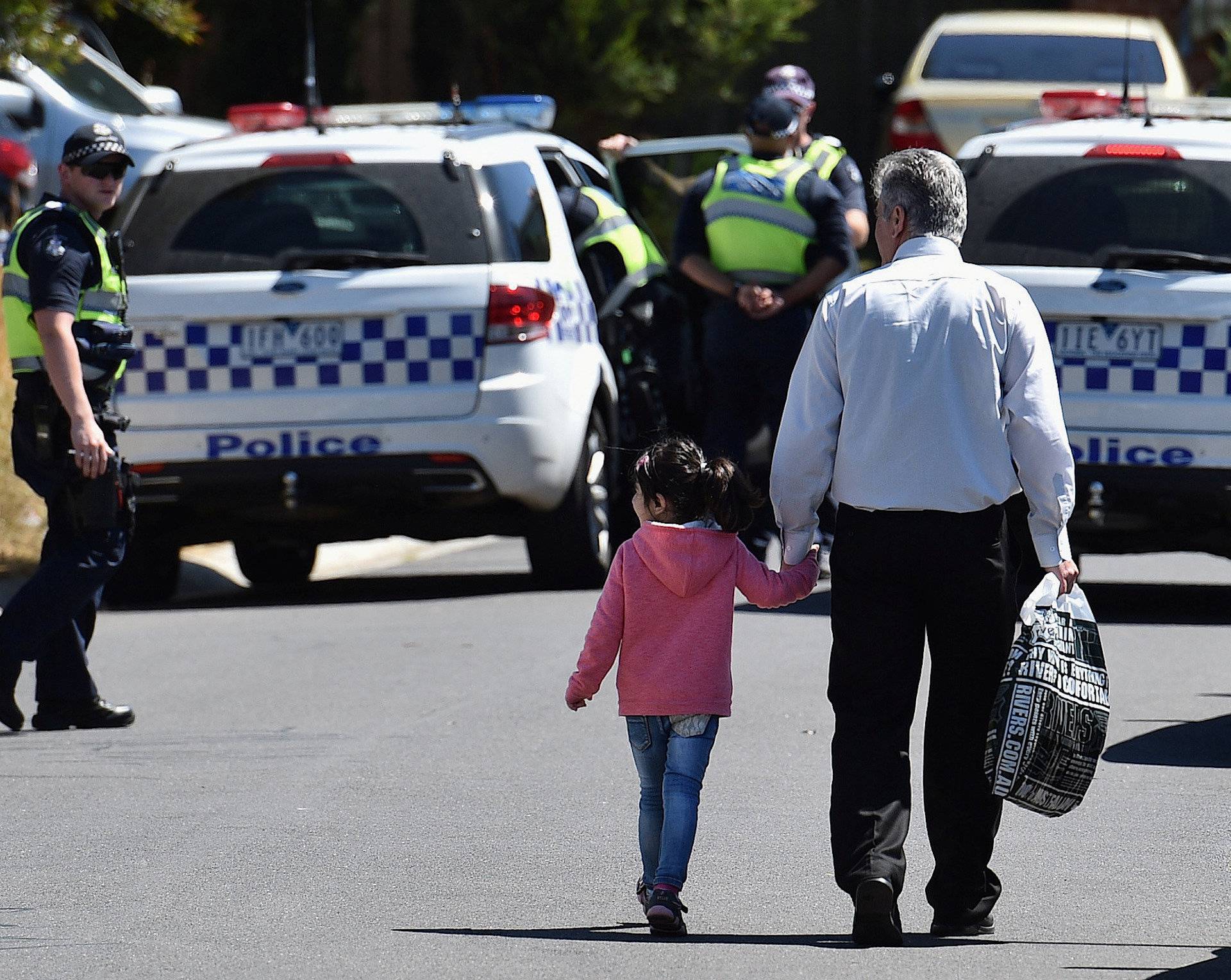 A man and a girl walk towards policemen as they block the road during the search of a house in the Melbourne suburb of Meadow Heights, Australia