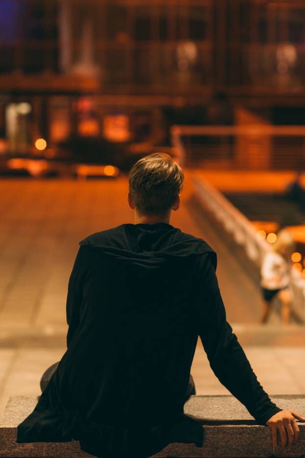 Guy sitting in night street, back view