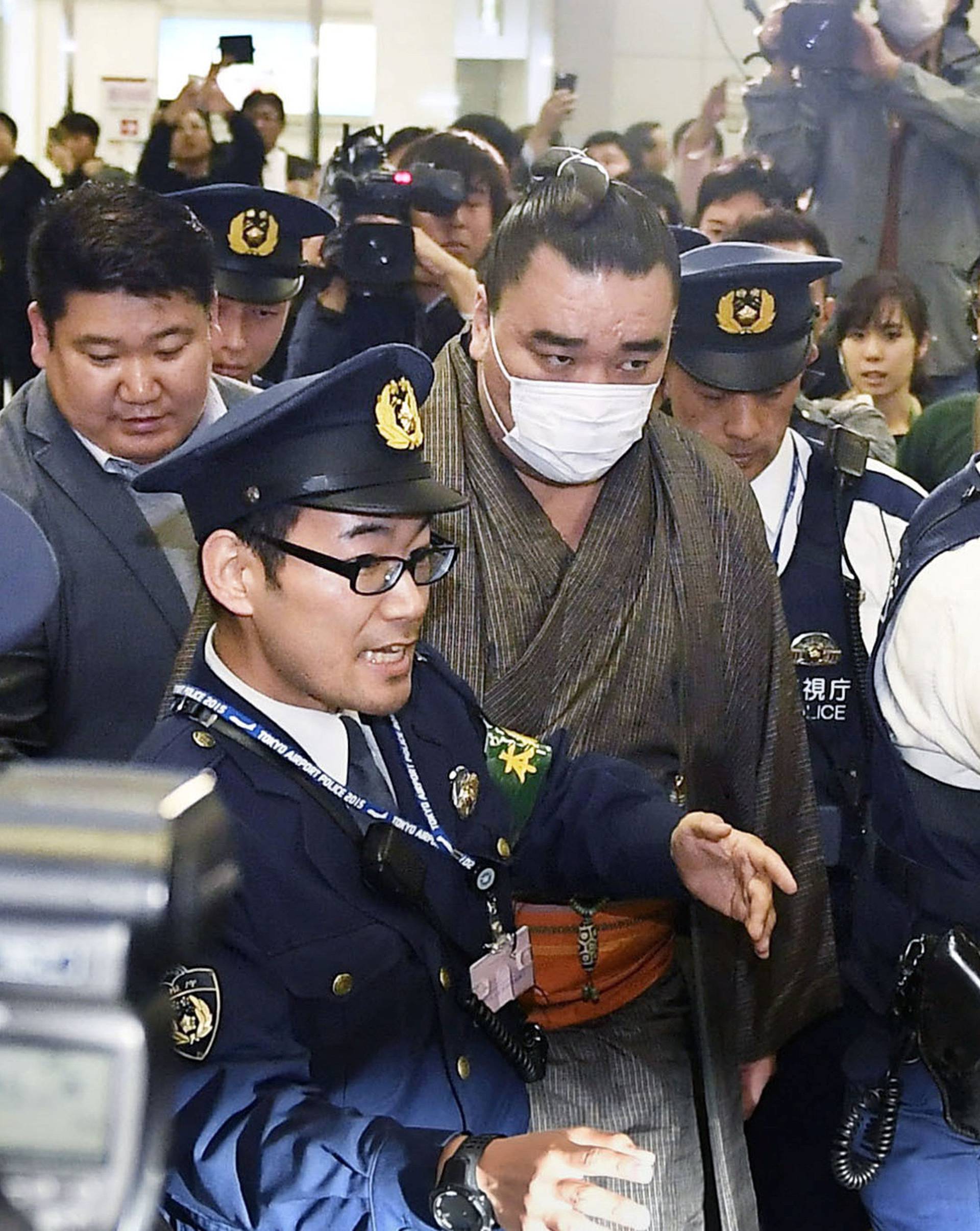 Mongolian-born grand sumo champion Yokozuna Harumafuji is escorted by police officers upon his arrival at Haneda airport in Tokyo