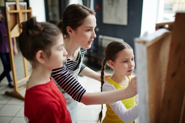 Portrait,Of,Young,Teacher,Helping,Children,To,Paint,On,Easels