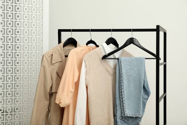 Rack with different stylish women`s clothes near light wall indo