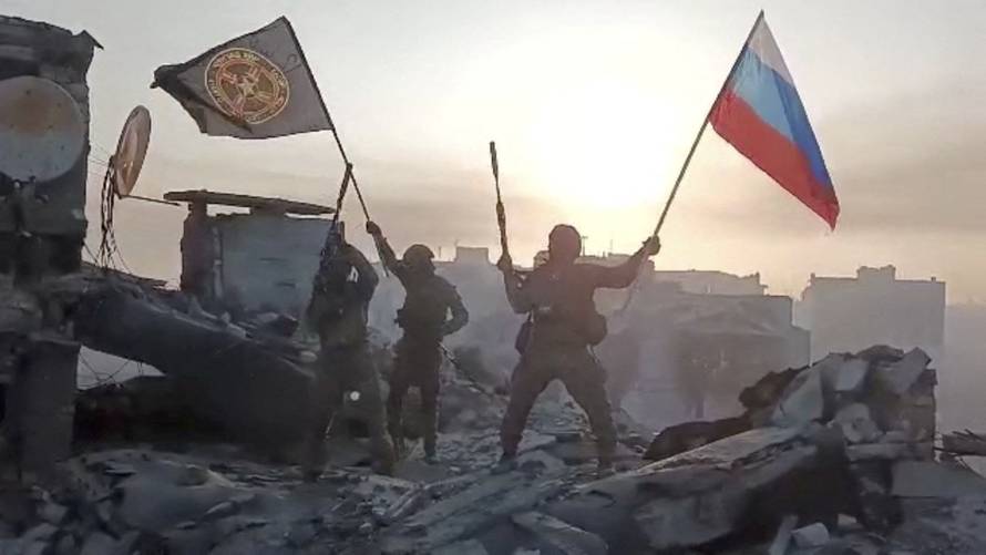 Wagner mercenary group fighters wave flags on top of a building in an unidentified location