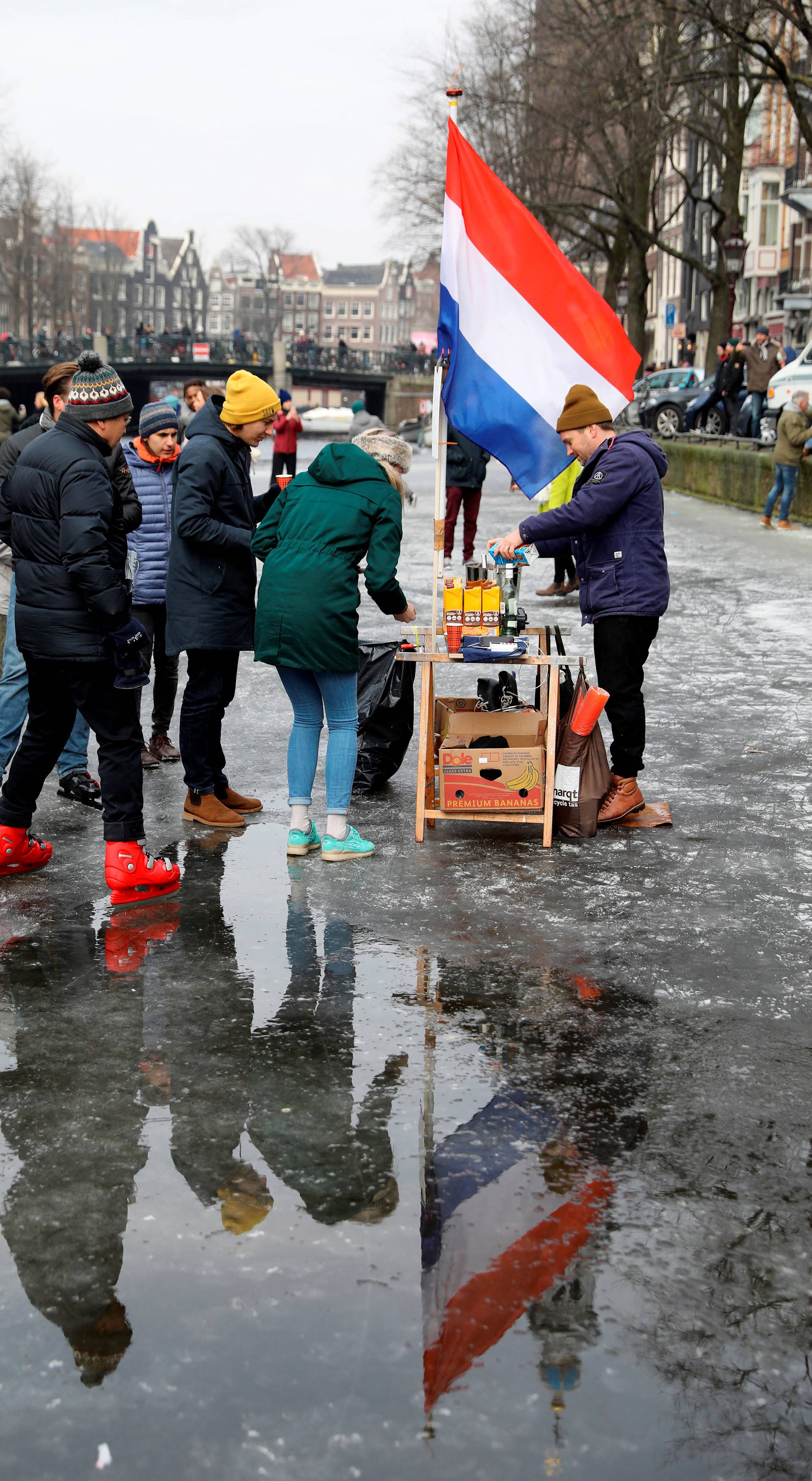 A vendor of hot chocolate watches as ice skaters skate and walk on the frozen Prinsengracht canal during icy weather in Amsterdam