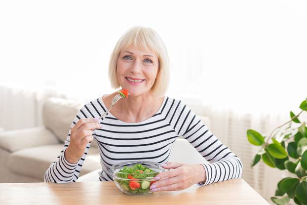 Happy senior lady eating fresh salad at home