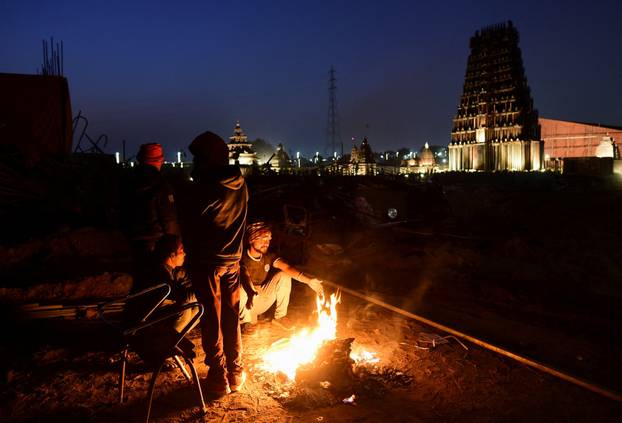 Construction workers sit beside a fire to keep themselves warm after a day's work ahead of the "Kumbh Mela", or the Pitcher Festival, in Prayagraj