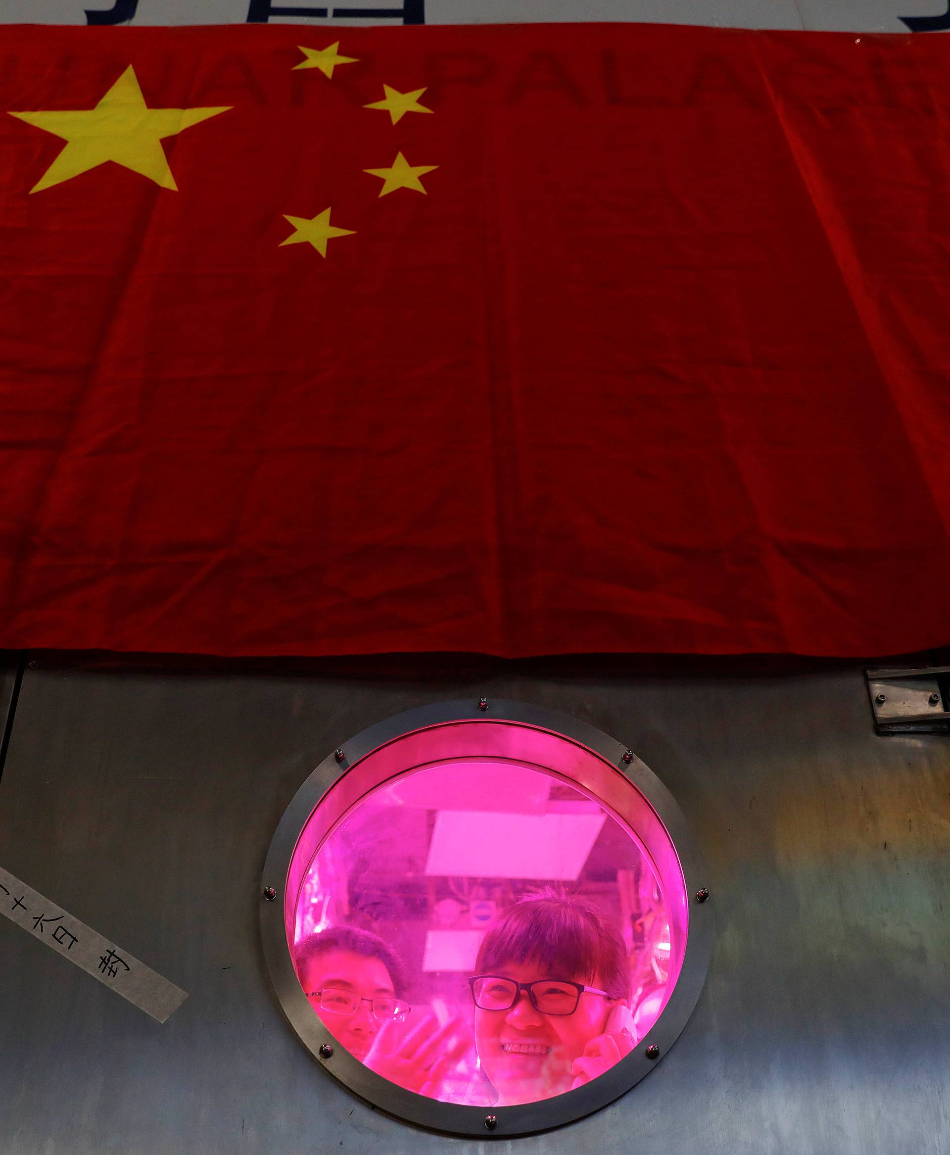 A volunteer waves to a member of staff from inside a simulated space cabin in which she temporarily lives with others as a part of the scientistic Lunar Palace 365 Project, at Beihang University in Beijing