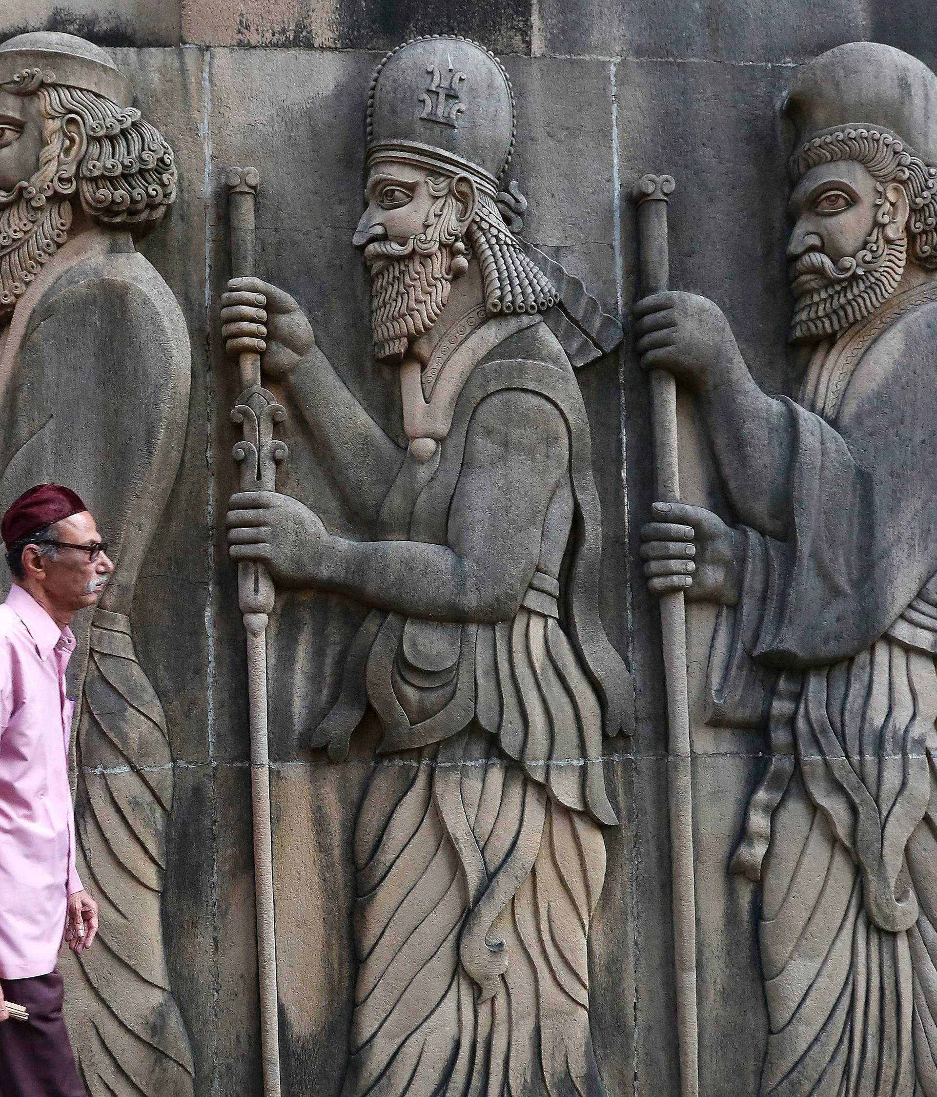 A Parsi man walks past a wall of a Parsi fire temple featuring huge carvings of ancient priests in Mumbai