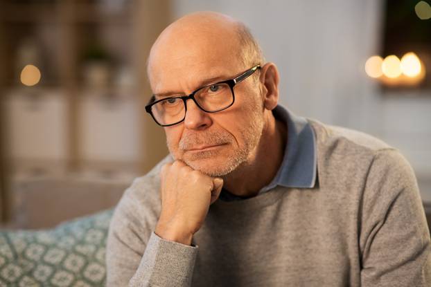 sad senior man in glasses thinking at home