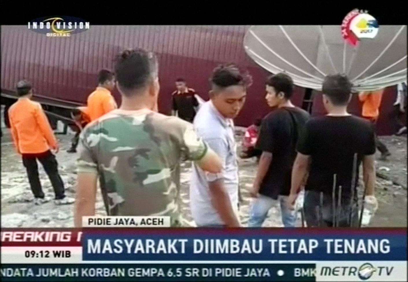 People stand next to a rescue operation conducted following an earthquake in Pidie Jaya, Aceh, Indonesia in this still frame taken from video