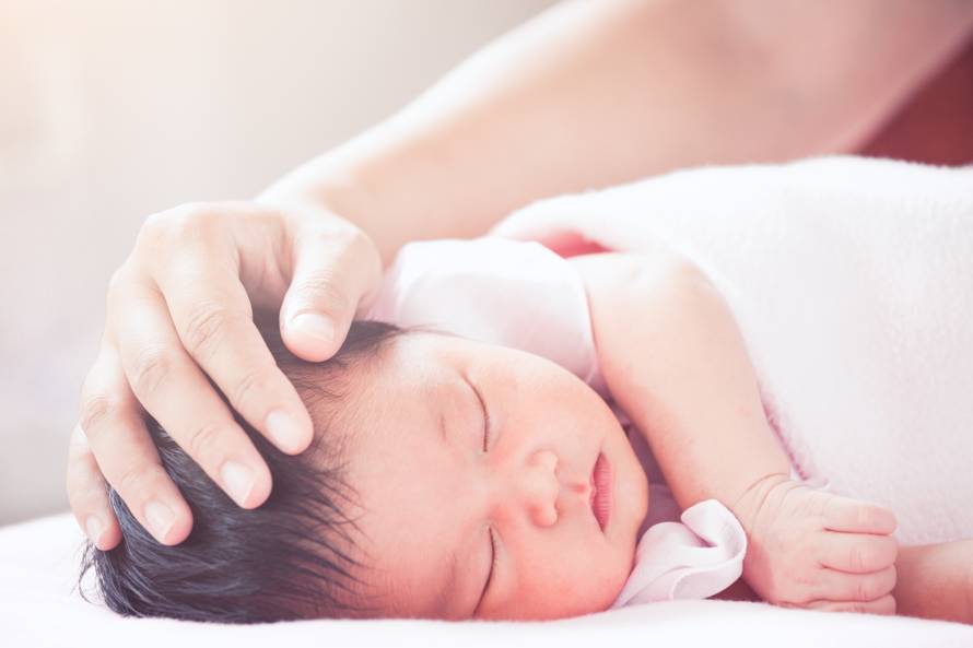 Mother hand touching asian newborn baby girl head while she slee