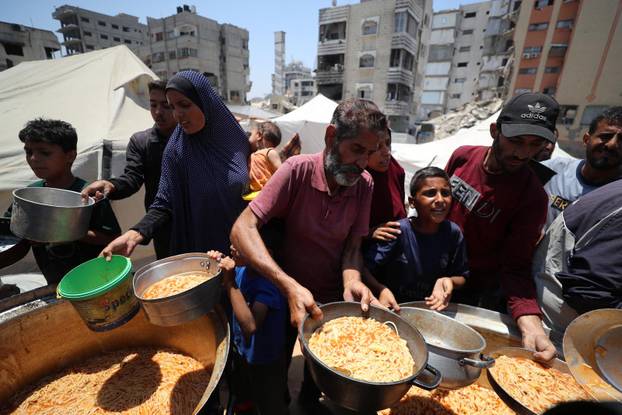 Palestinians wait to receive food cooked by a charity kitchen, in Gaza City