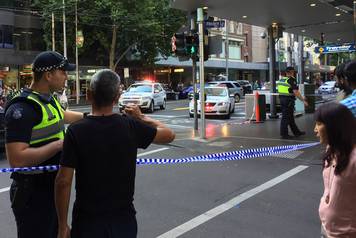 Police officers stand guard as members of the public stand behind police tape after the arrest of the driver of a vehicle that ploughed into pedestrians at a crowded intersection near the Flinders Street train station in central Melbourne