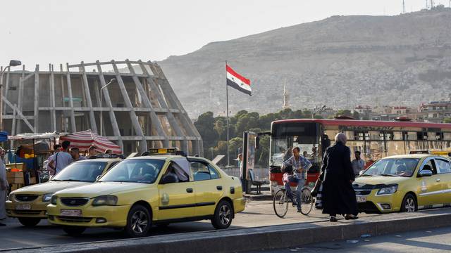 The Syrian national flag flutters near taxi cars in Damascus
