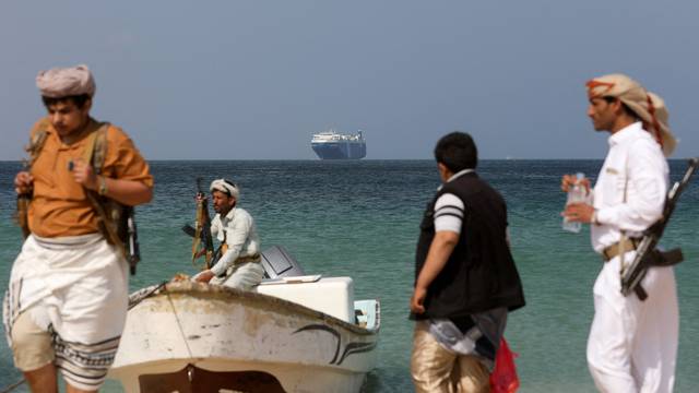 FILE PHOTO: Armed men stand on the beach as the Galaxy Leader commercial ship, seized by Yemen's Houthis last month, is anchored off the coast of al-Salif