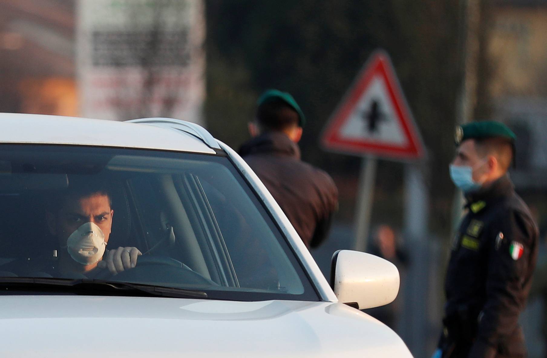 A man wearing a face mask drives past members of the Guardia di Finanza, amid a coronavirus outbreak in northern Italy, in Casalpusterlengo