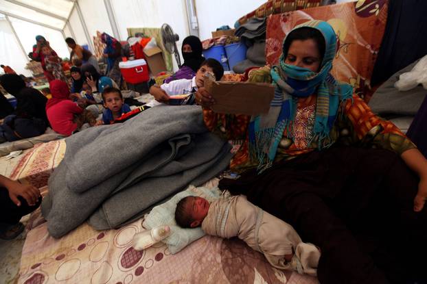A displaced woman sits next to her sleeping child at a refugee camp in the Makhmour area near Mosul