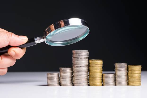 Closeup,Hand,With,Magnifying,Glass,Analyze,On,Money,Heap,Coins