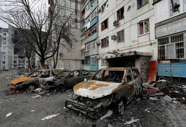 FILE PHOTO: Destroyed cars are seen in front of a damaged apartment building in the besieged city of Mariupol