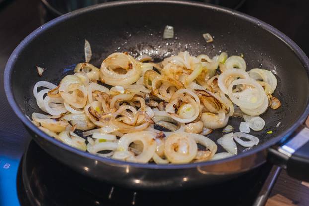 Closeup shot of sliced onion pieces frying in a pan with an oil
