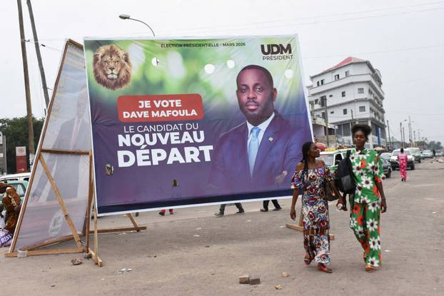 People walk past a campaign billboard of presidential candidate Uphrem Dave Mafoula, in Brazzaville