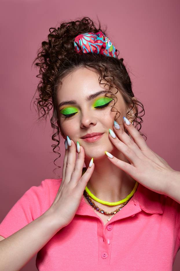 Young woman on pink background with green closed eyes makeup and