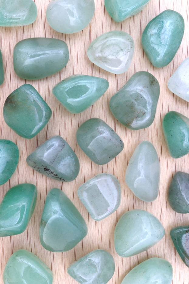 Green Aventurine rare jewel on brown varnished wood texture. Sparse mineral pebbles background.