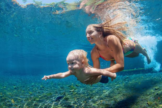 Mother with child swim and dive underwater in sea pool