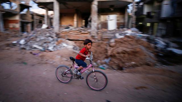 A boy rides his bicycle near the rubble of a house which was destroyed by Israeli air strikes during the Israel-Hamas fighting, in Gaza Strip