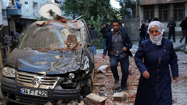 People walk past a damaged car after a blast in the Kurdish-dominated southeastern city of Diyarbakir