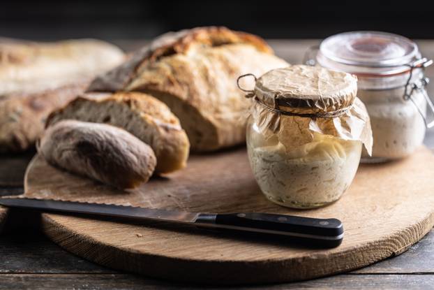 Rye sourdough ripened in a jar together with fresh bread on a cutting board.