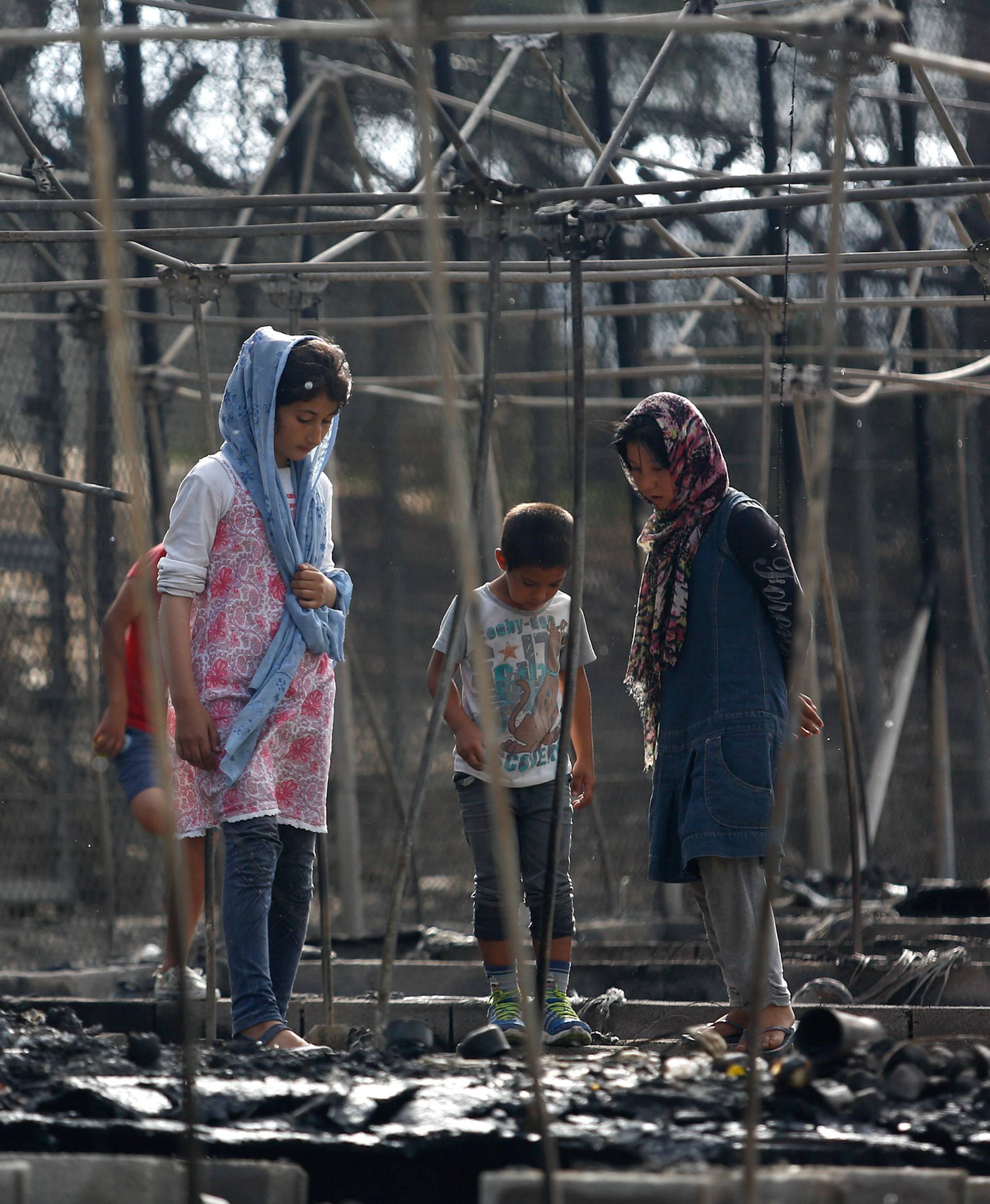 Migrants stand among the remains of a burned tent at the Moria migrant camp, after a fire that ripped through tents and destroyed containers during violence among residents, on the island of Lesbos