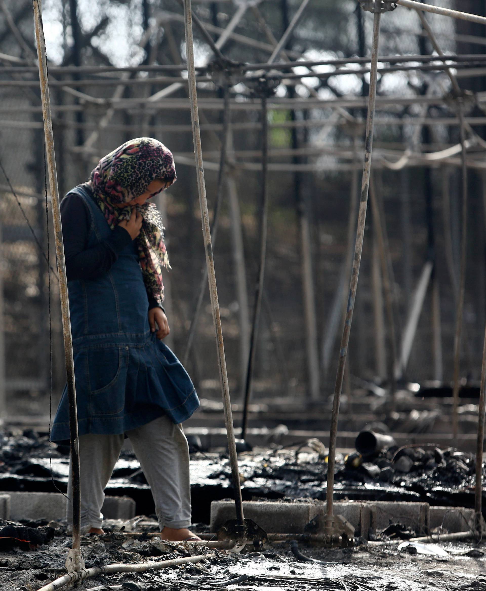 A migrant stands among the remains of a burned tent at the Moria migrant camp, after a fire that ripped through tents and destroyed containers during violence among residents, on the island of Lesbos