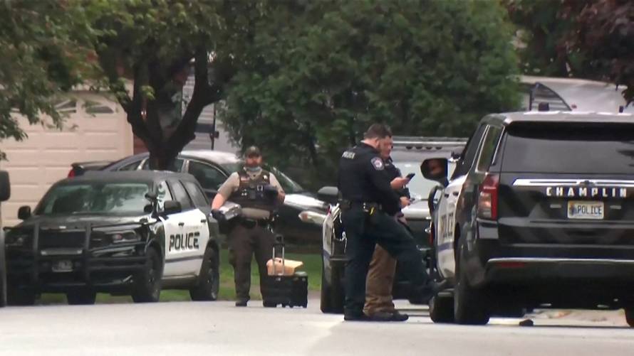 Police stand at a crime scene as they searched for a suspect posing as a police officer who shot two Democratic state lawmakers
