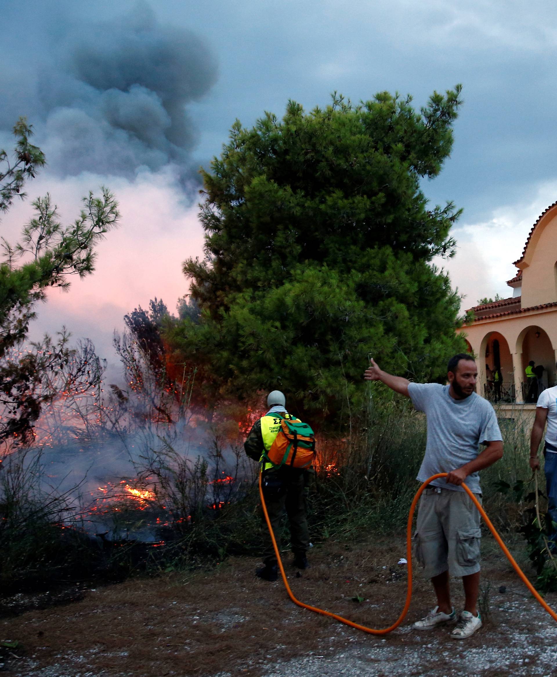 People try to extinguish a wildfire burning next to a church in the town of Rafina, near Athens