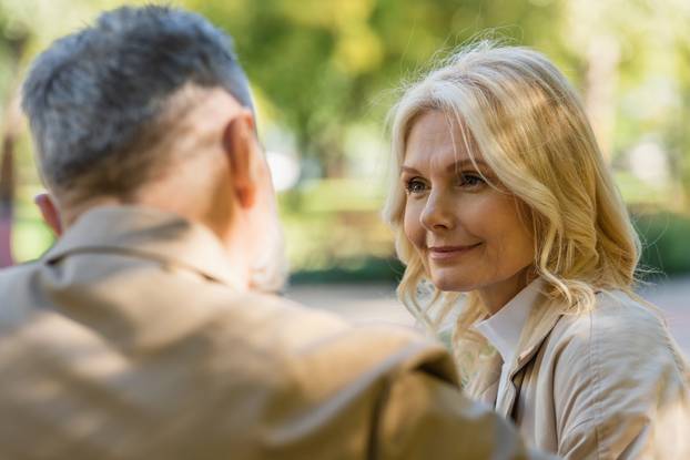 Smiling blonde woman looking at blurred husband in spring park