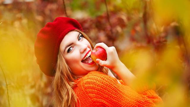 Lovely girl in beret and sweater, holding ripe apple and smiling
