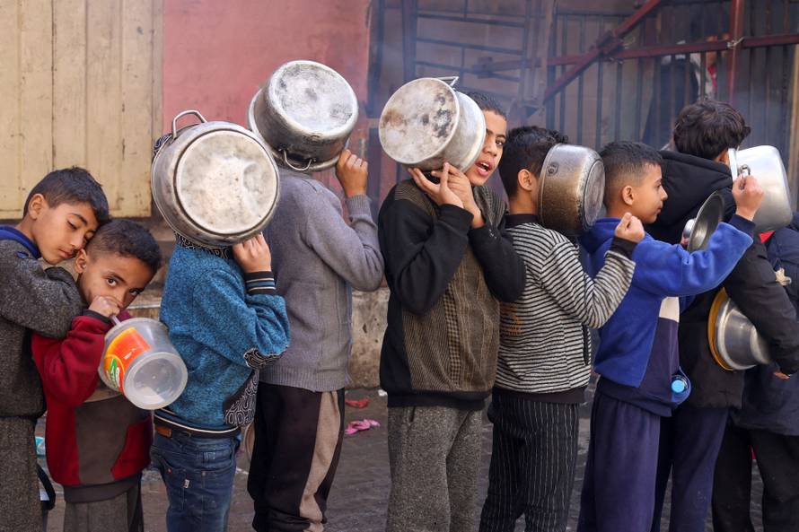 FILE PHOTO: Palestinian children carry pots as they queue to receive food cooked by a charity kitchen, in Rafah in the southern Gaza Strip