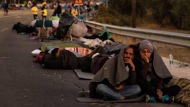 Couple sits covered with a blanket as refugees and migrants camp on a road following a fire at the Moria camp on the island of Lesbos