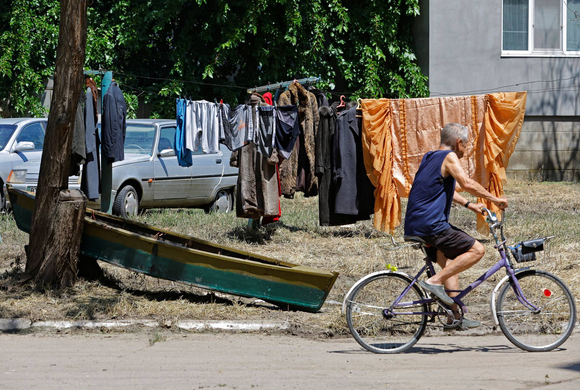A man rides his bicycle past a boat in the yard of an apartment building in Hola Prystan