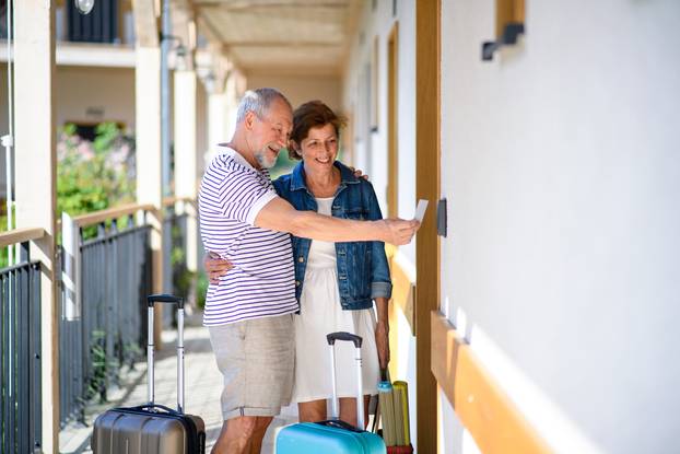 Senior,Couple,With,Luggage,Outside,Apartment,On,Holiday.