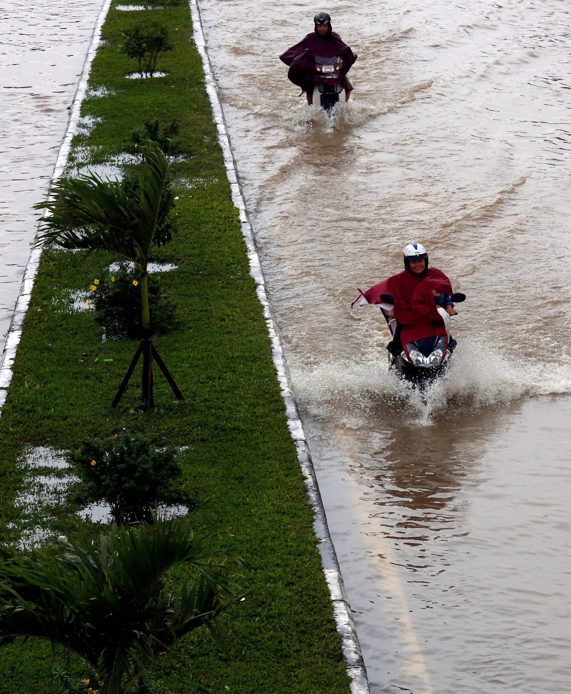 People ride motorcycles along flooded road after typhoon Damrey hits Vietnam in Hue city