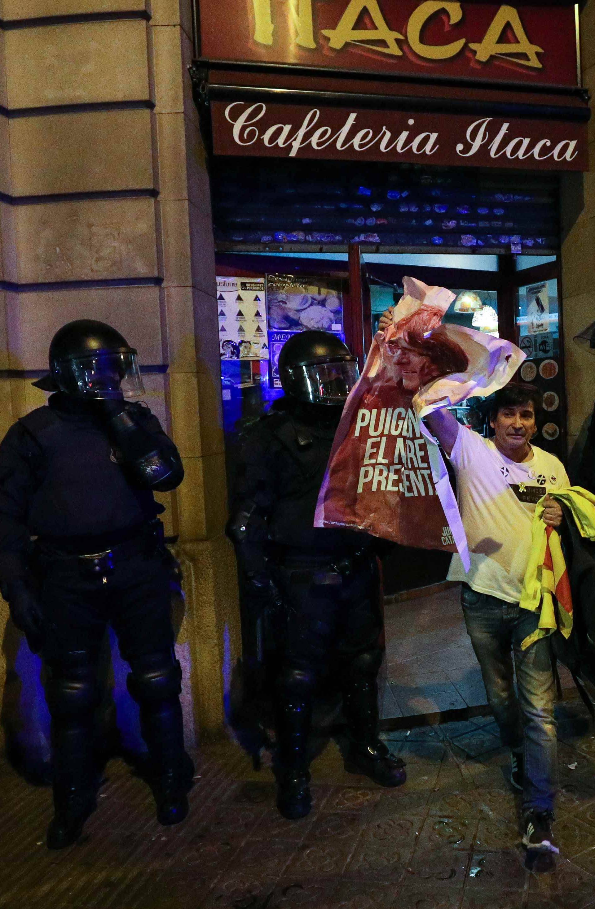 A protestor holds up a poster of former Catalan president Carles Puigdemont as he leaves a cafe during skirmishes with police after Puigdemont was detained in Germany,  in Barcelona