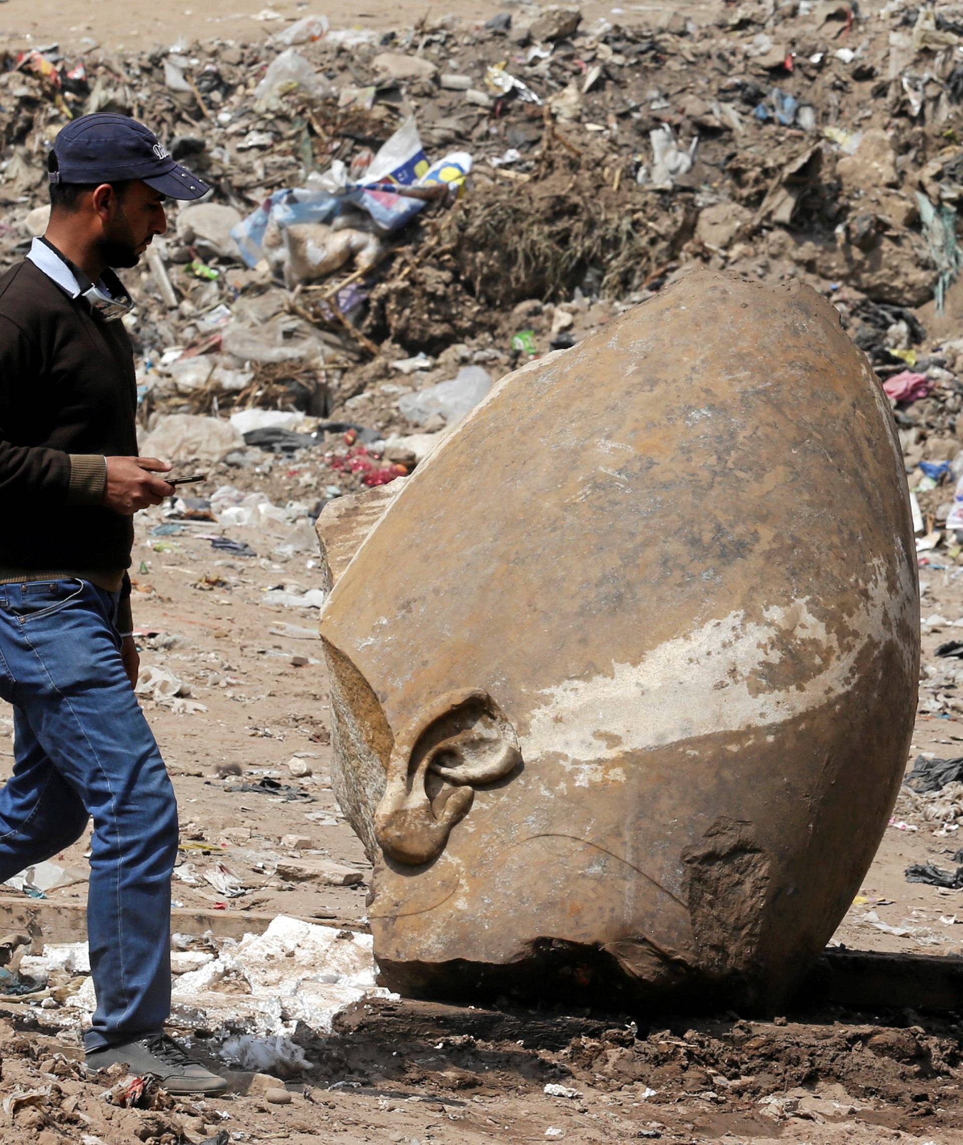 A man passes by what appears to be the head of an unearthed statue that workers say depicts Pharaoh Ramses II, in Cairo