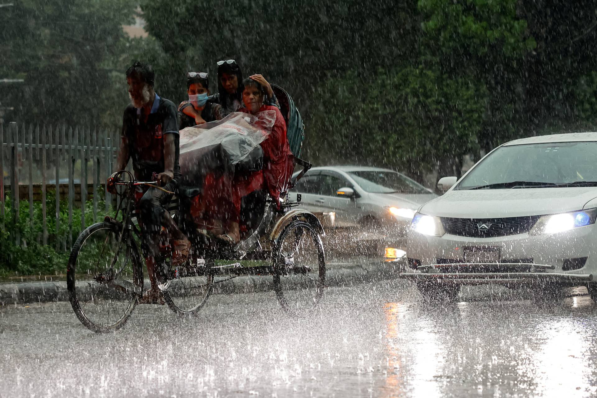 People riding on a rickshaw during a downpour in Dhaka