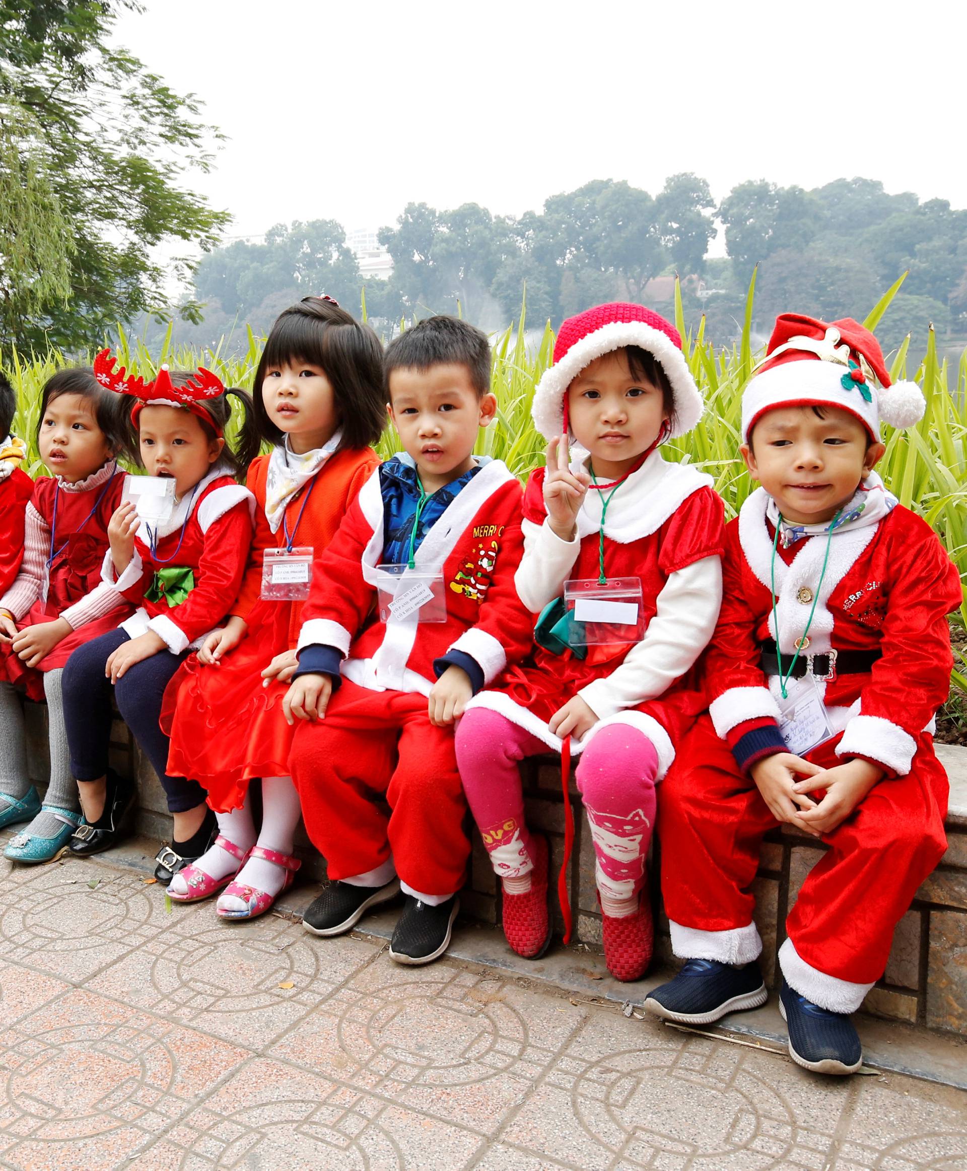 Children wearing Santa Claus outfits sit along Hoan Kiem Lake in Hanoi, Vietnam