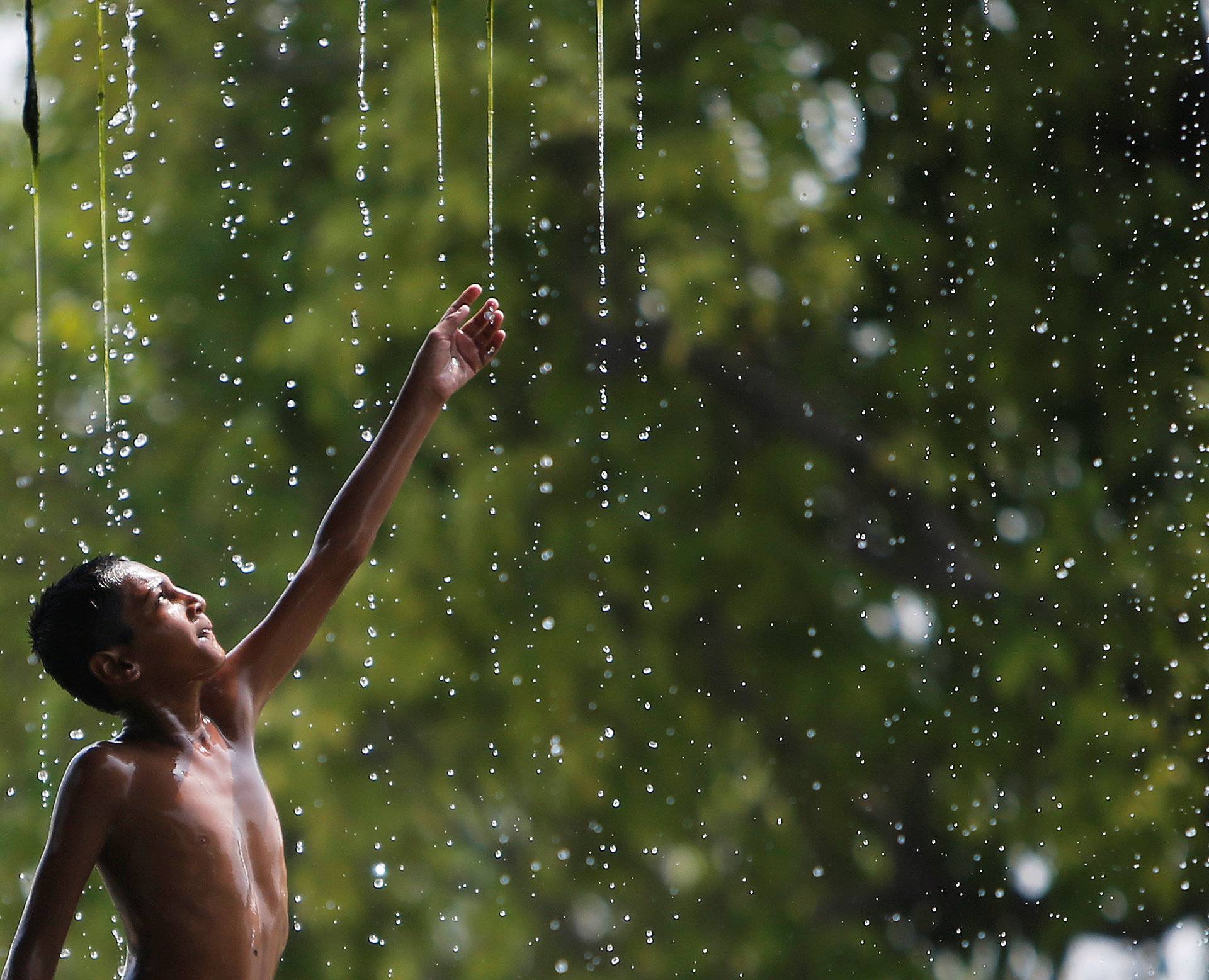 A boy cools off under a water fountain on a hot summer day in New Delhi