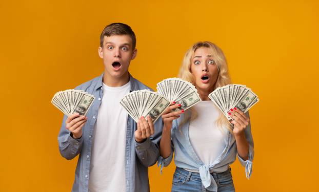 Shocked young couple holding lots of money in hands