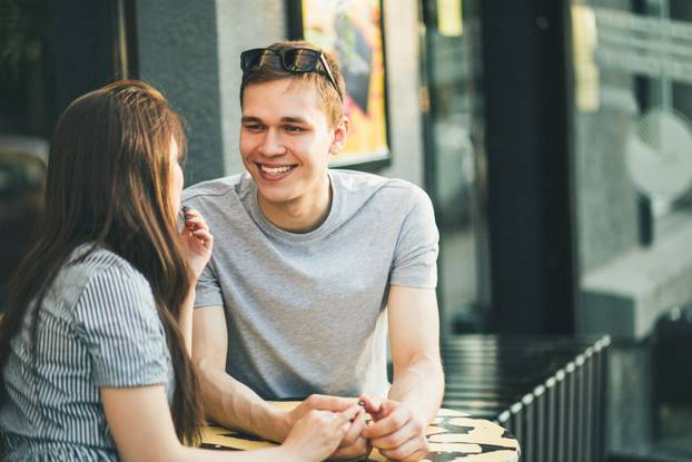Happy young couple in love teenagers friends dressed in casual style sitting together on city street